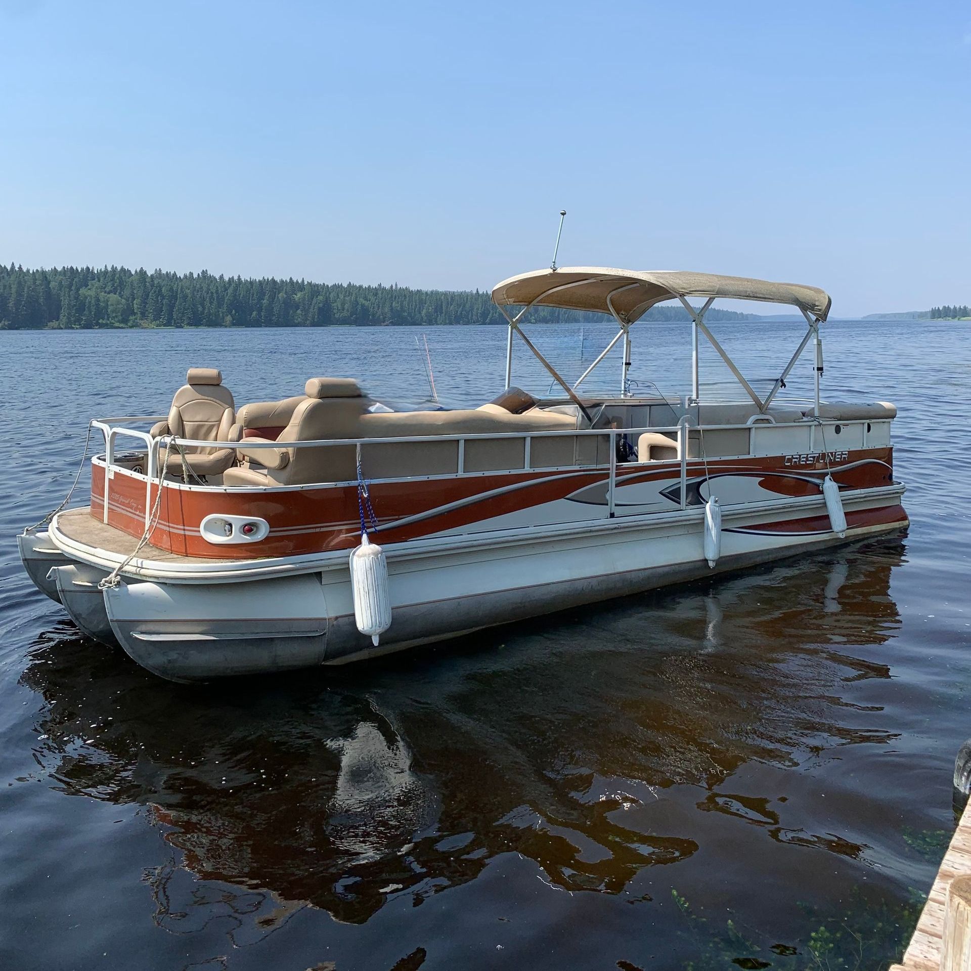 A pontoon boat is docked at a dock on a lake