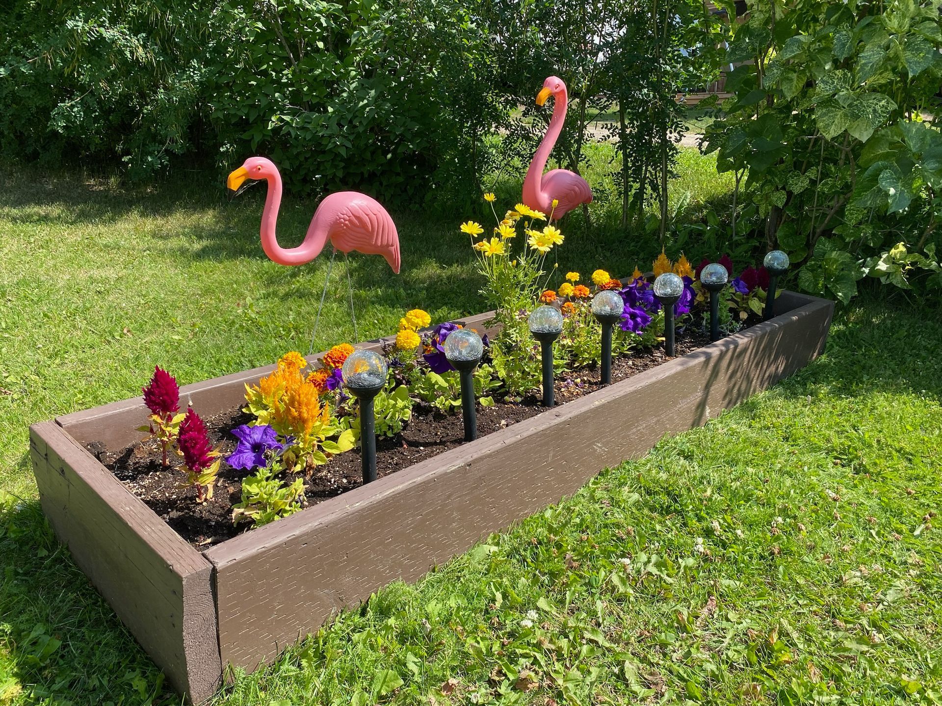 A planter filled with flowers and flamingos in a yard.