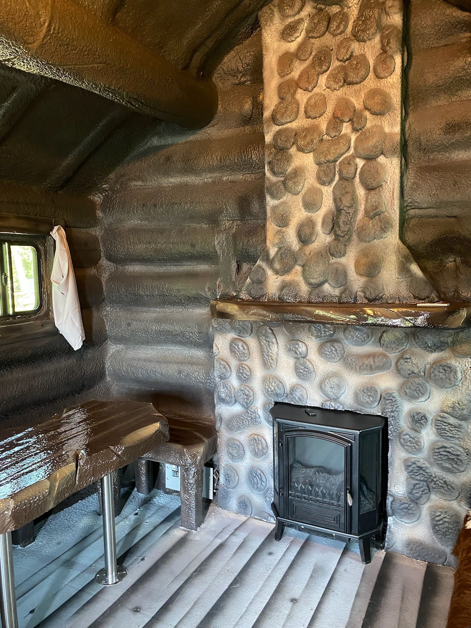 A log cabin with a wood stove and a stone fireplace.