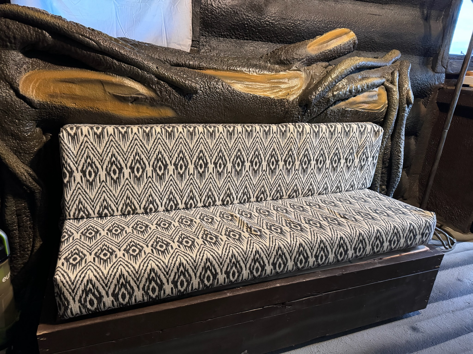 A couch with a patterned cushion is sitting next to a statue.