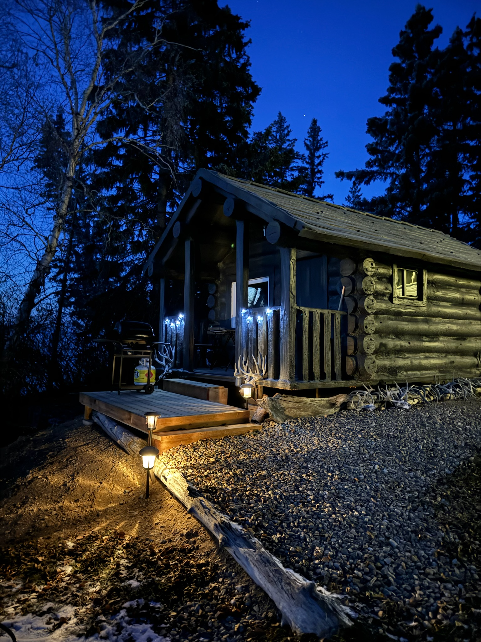 A small log cabin is lit up at night in the woods.