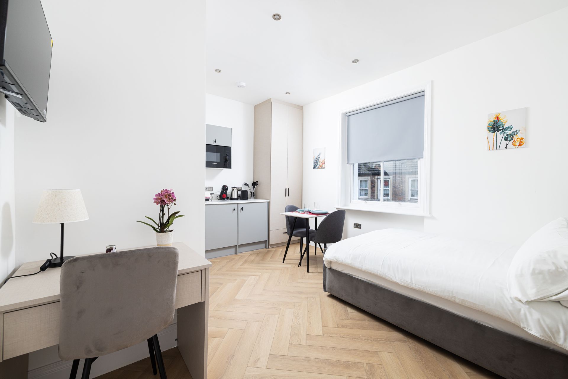 Bright minimalist bedroom with white walls, bed, desk, chair, and window blinds