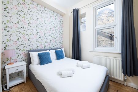 Bright bedroom with white bed, blue pillows, floral wallpaper, and a window with gray curtains.