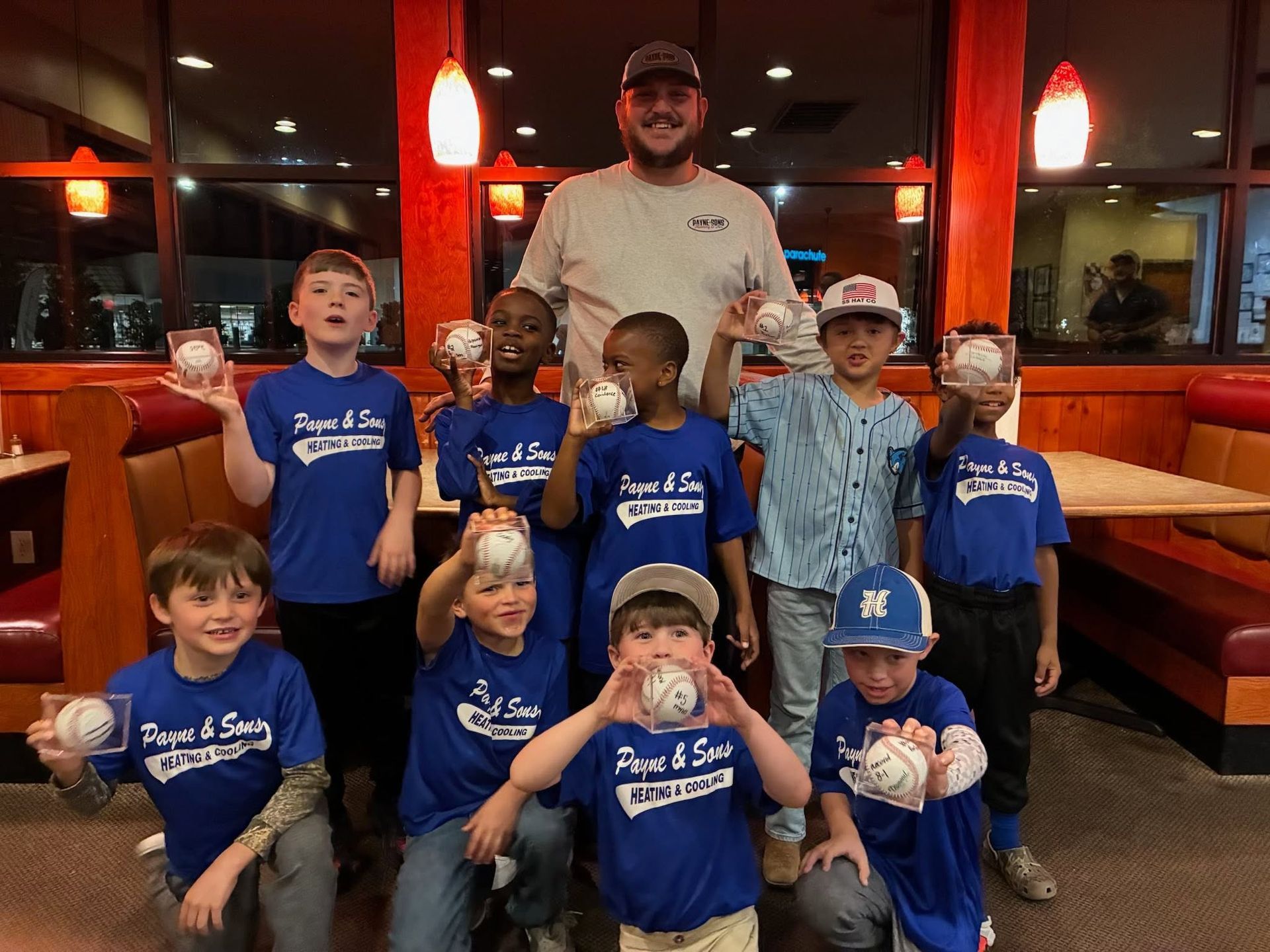 Youth baseball team with coach posing in a restaurant booth area, wearing blue shirts and caps