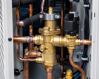 Copper and brass plumbing valves and pipes inside a utility panel, with black wiring on the right.