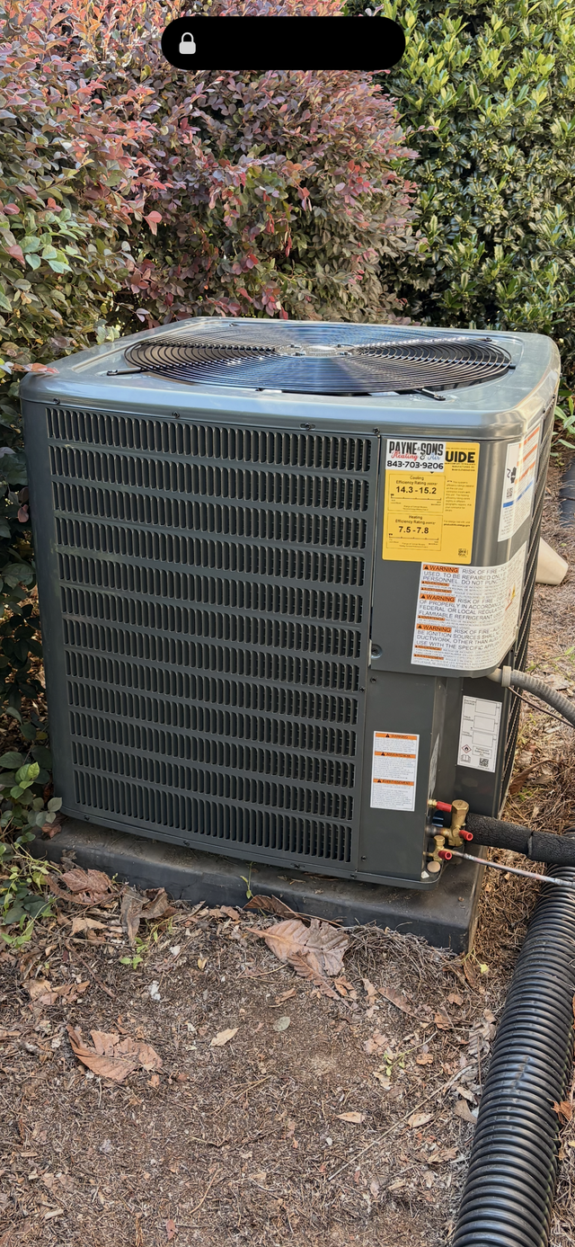 Outdoor air conditioner unit on a gravel bed beside a house, with bushes in the background.