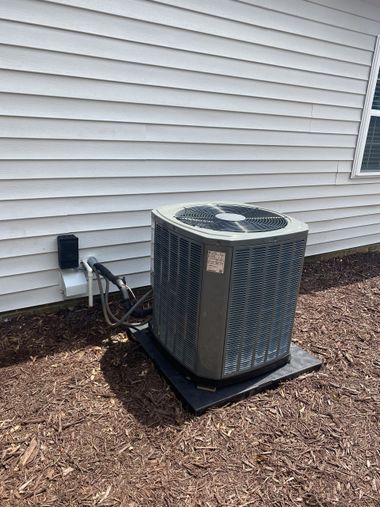 Outdoor air conditioner unit beside a house with white siding and mulch bed