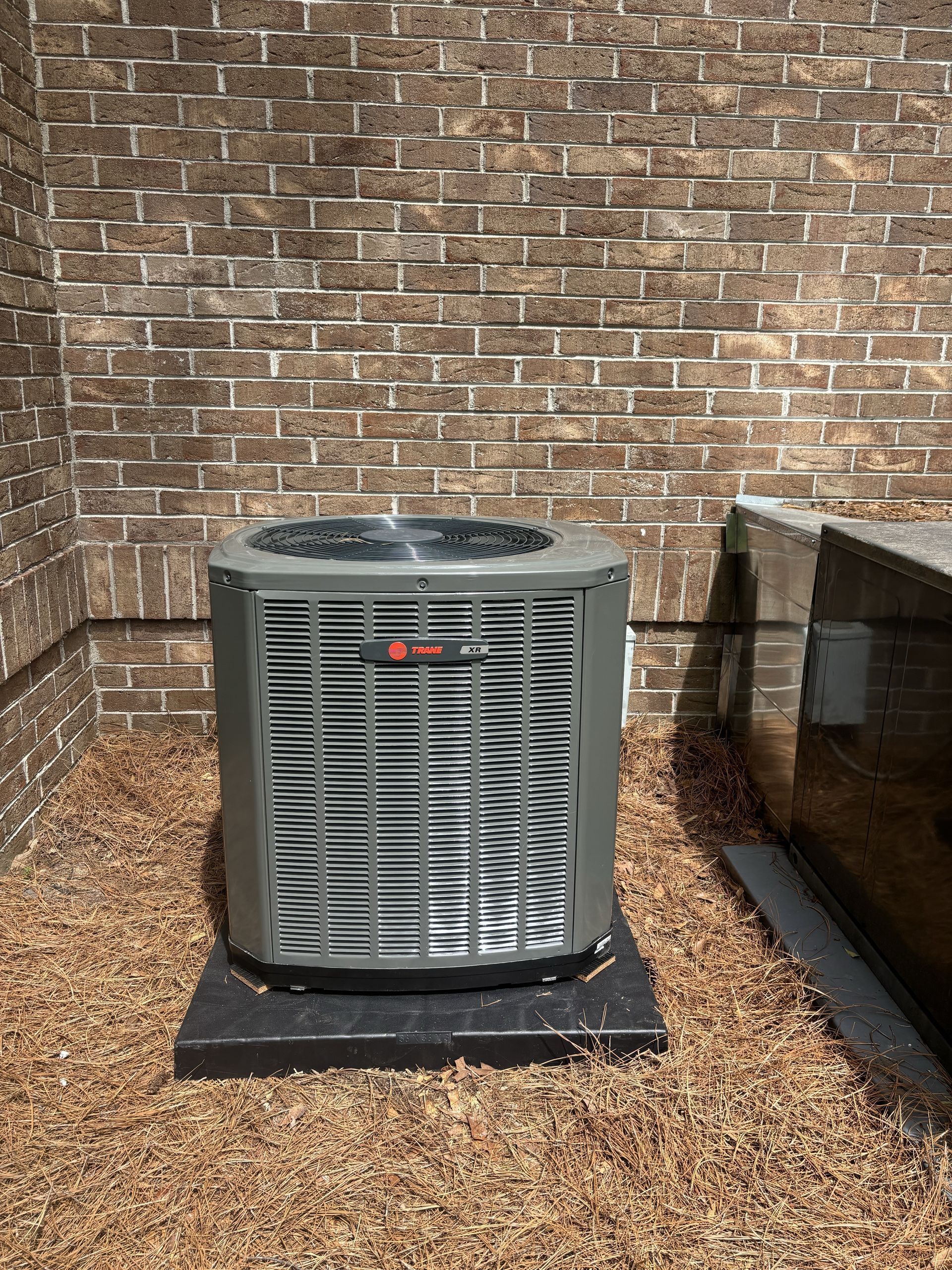Outdoor air conditioner unit beside a brick wall on a gravel pad