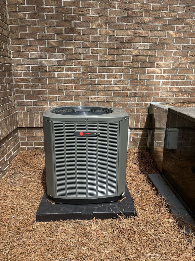Outdoor air conditioner unit beside a brick wall on a gravel pad