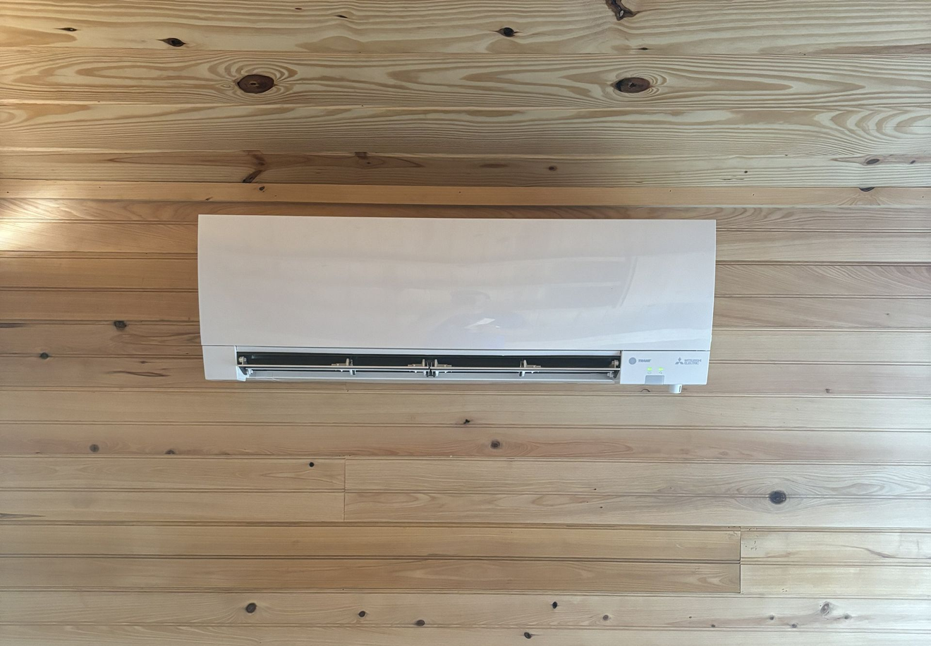Wall-mounted white air conditioner on a wood-paneled wall with gray wainscoting and an outlet below