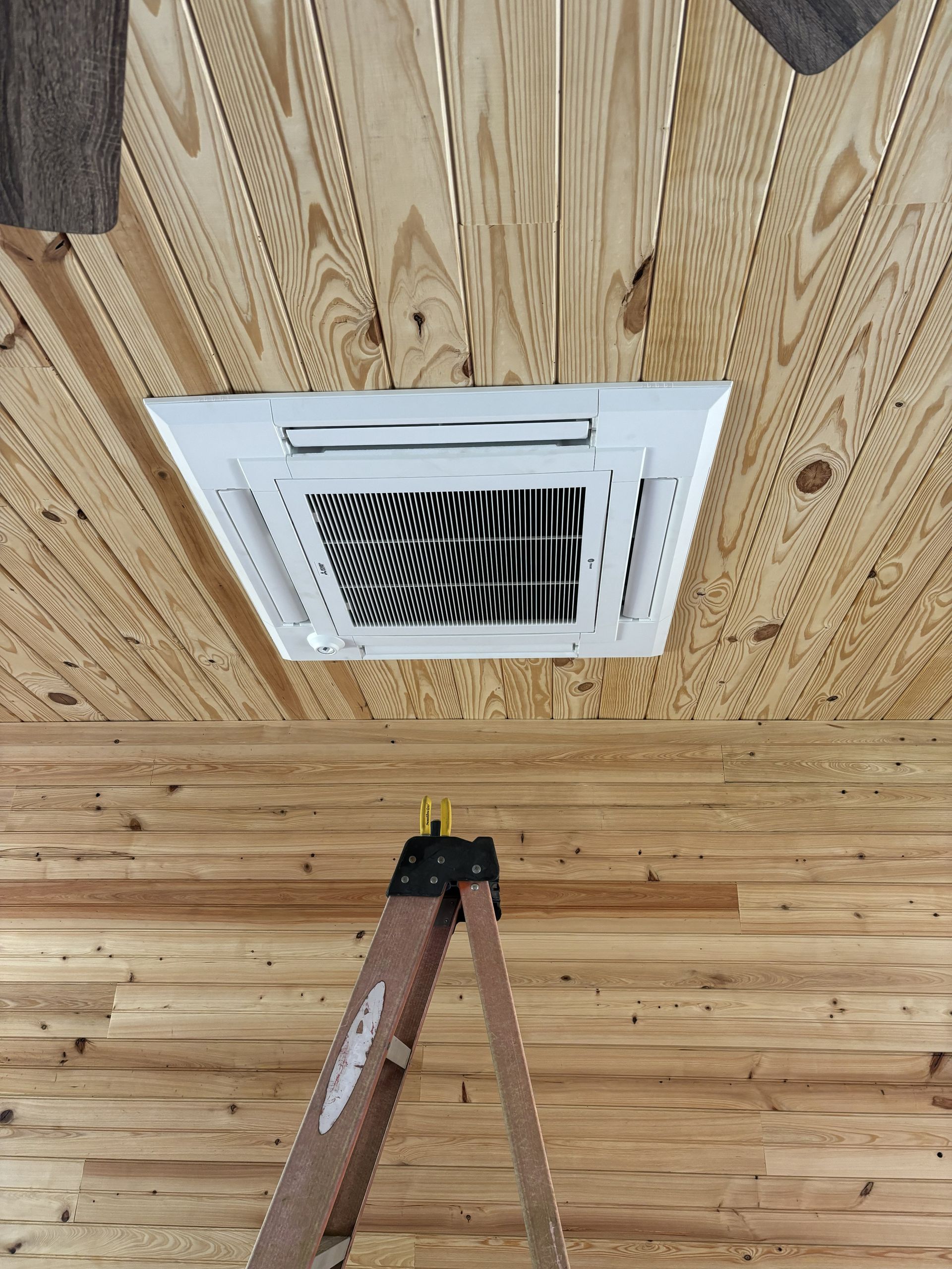 Ceiling air vent with white grille on wood-paneled ceiling above a ladder