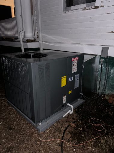 Outdoor HVAC unit beside a white brick wall, with piping and wet ground around it
