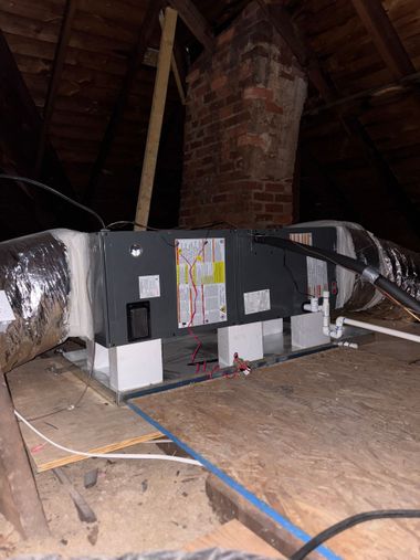 Attic HVAC unit with ducts and exposed brick chimney in a dim, unfinished attic