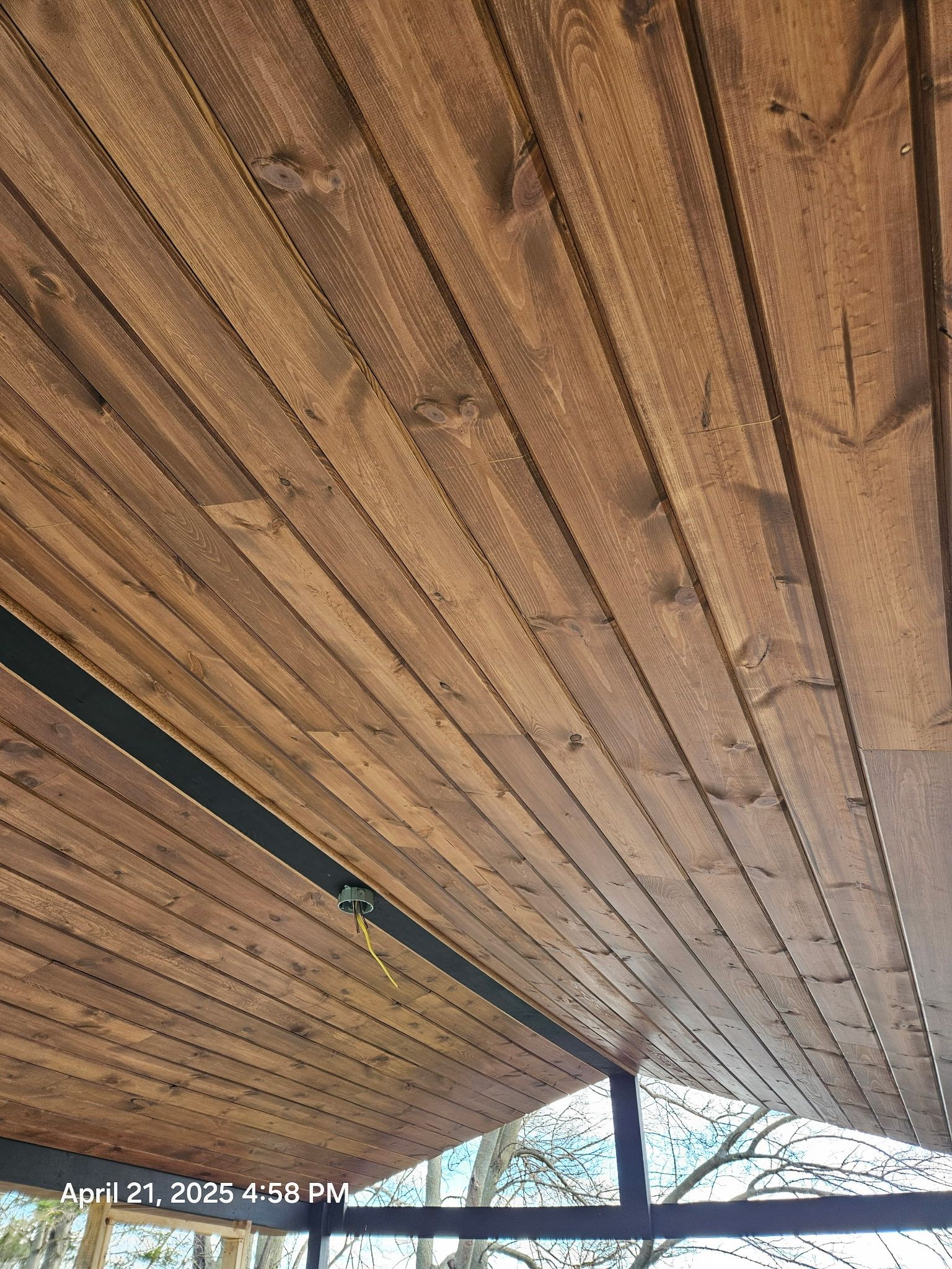 Wooden slatted roof viewed from below, with a dark support beam and bright sky at the edge.