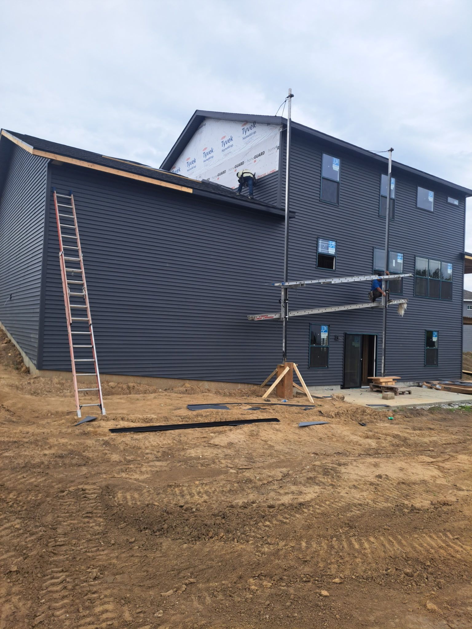 Damaged gray house exterior with a ladder leaning against it and exposed siding under repair