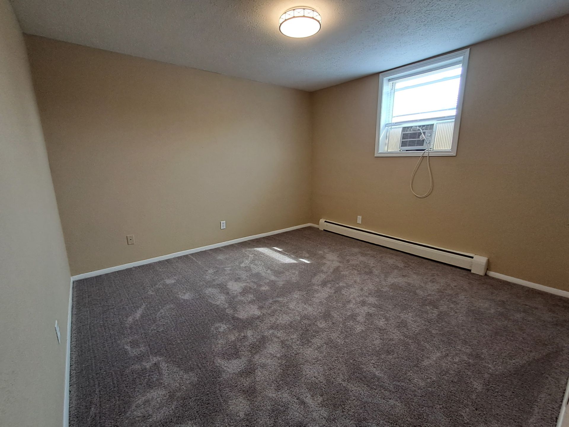 Empty beige bedroom with gray carpet, window air conditioner, and ceiling light