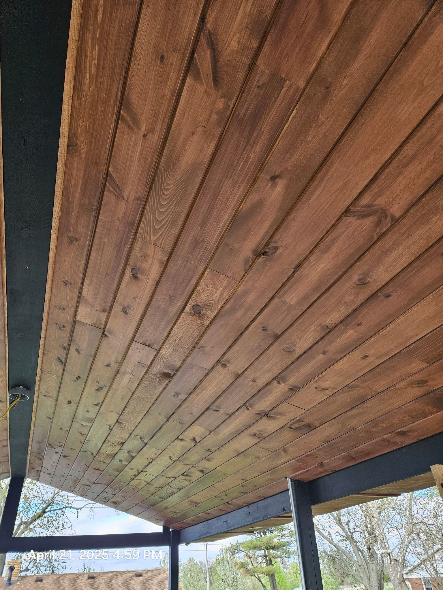 Wooden pavilion ceiling with dark support beams and trees visible beyond the open sides.