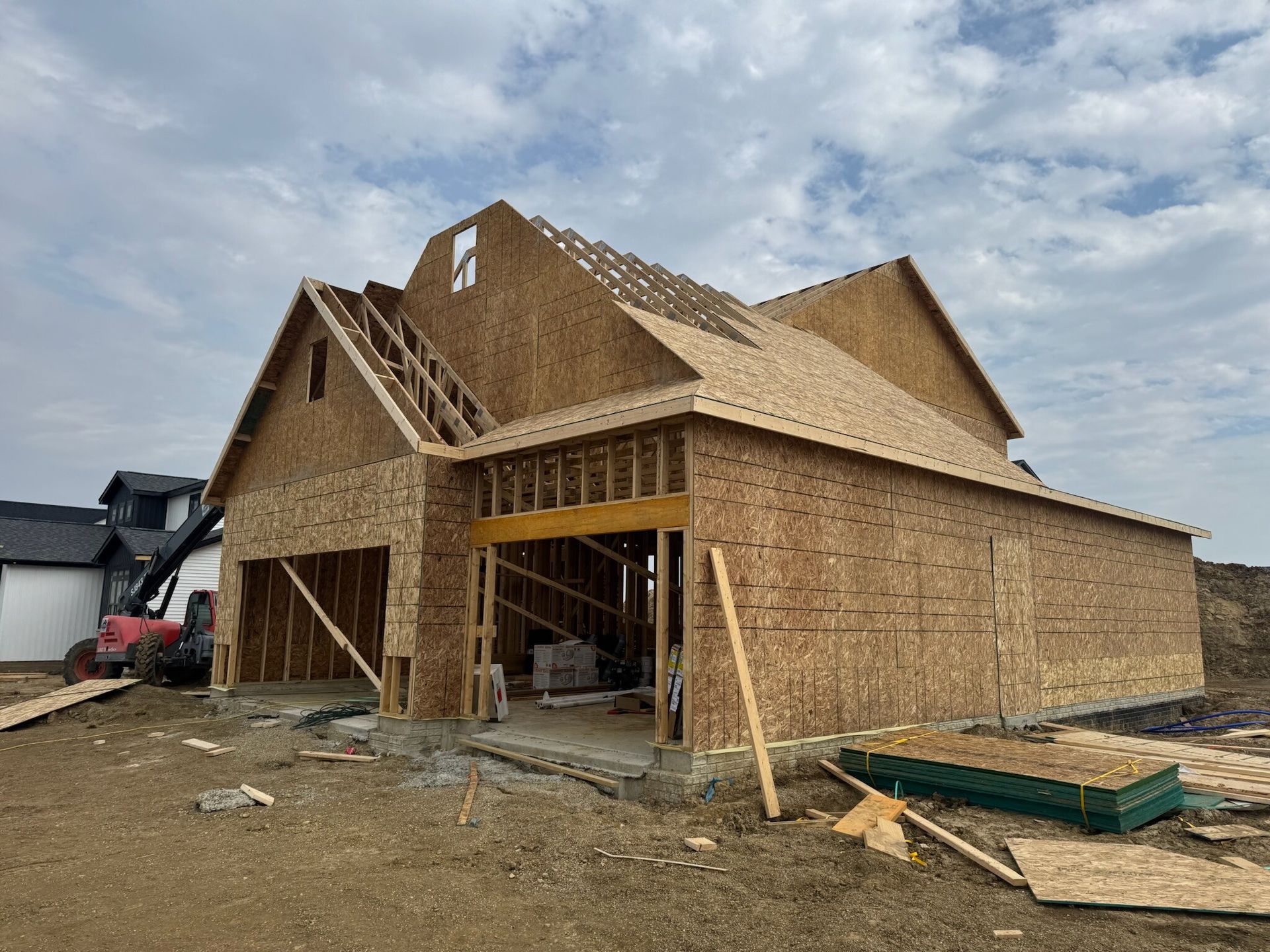 Partially framed house under construction with plywood sheathing and an excavator nearby
