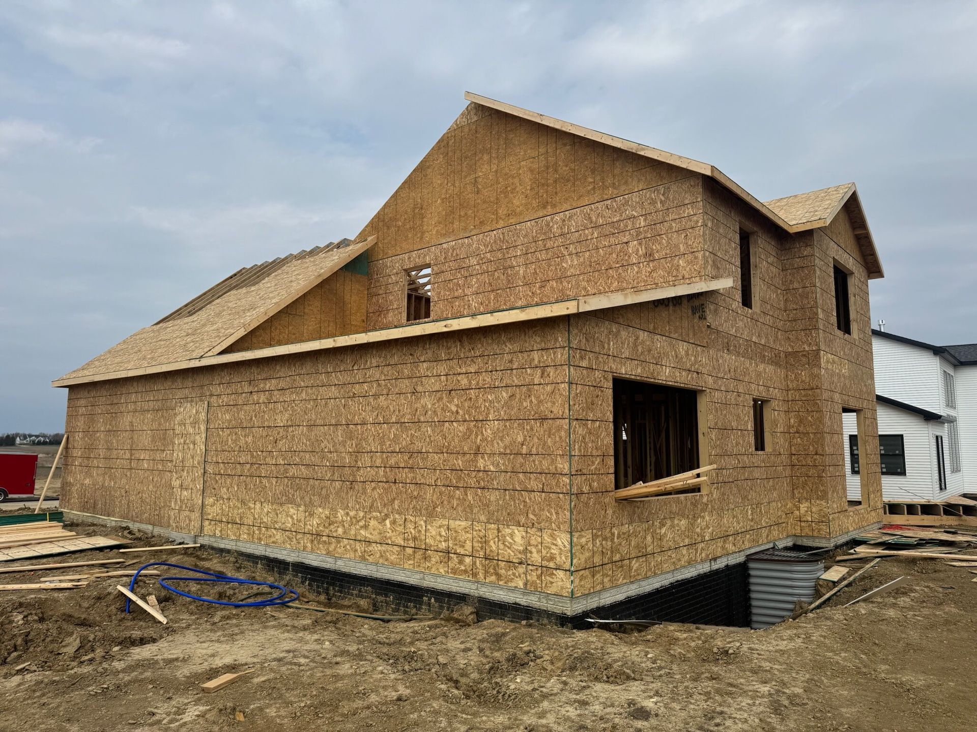 Partially built house wrapped in OSB sheathing on a muddy construction site