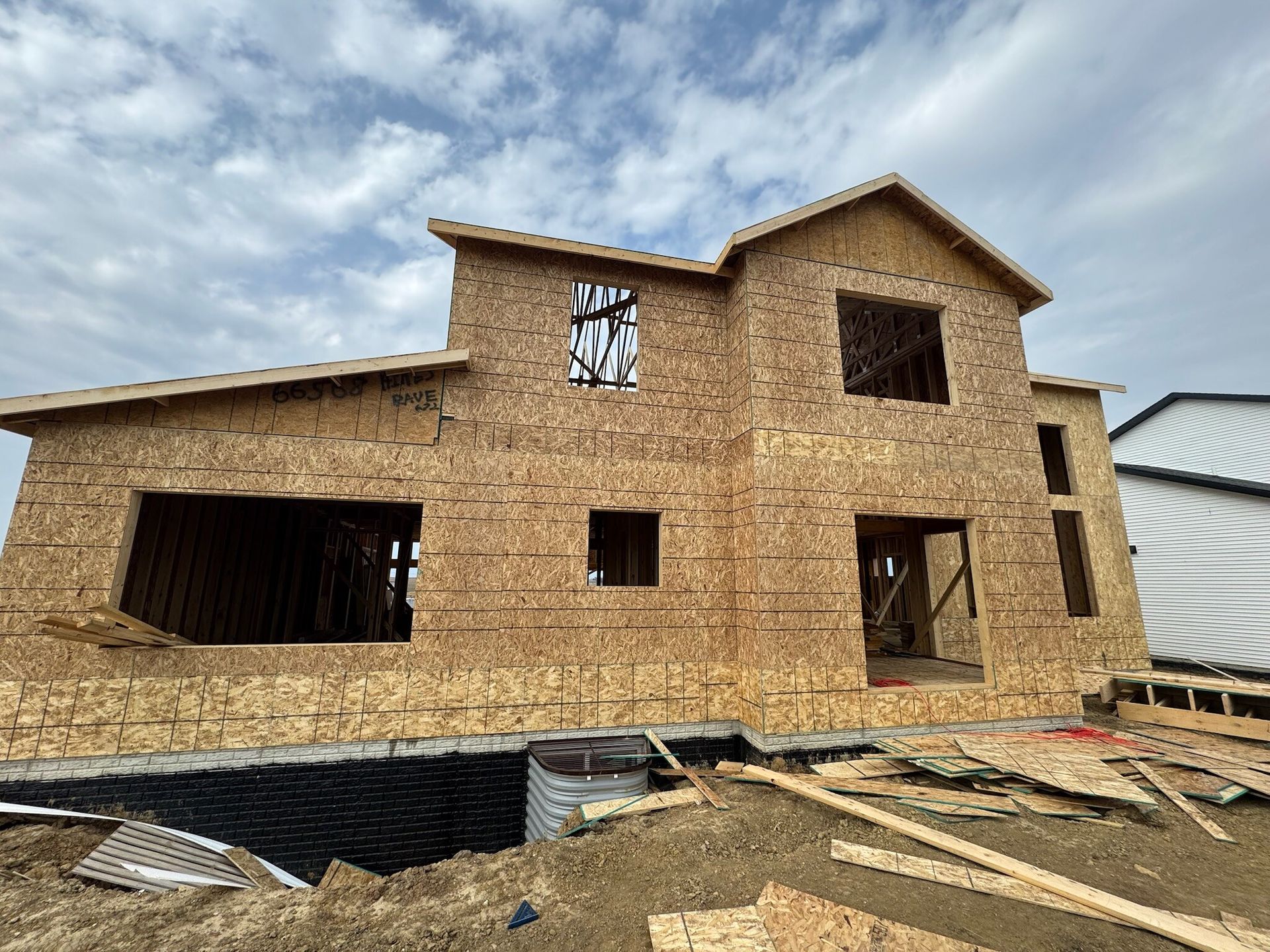 Partially built brick house with exposed framing and construction debris in front under a cloudy sky