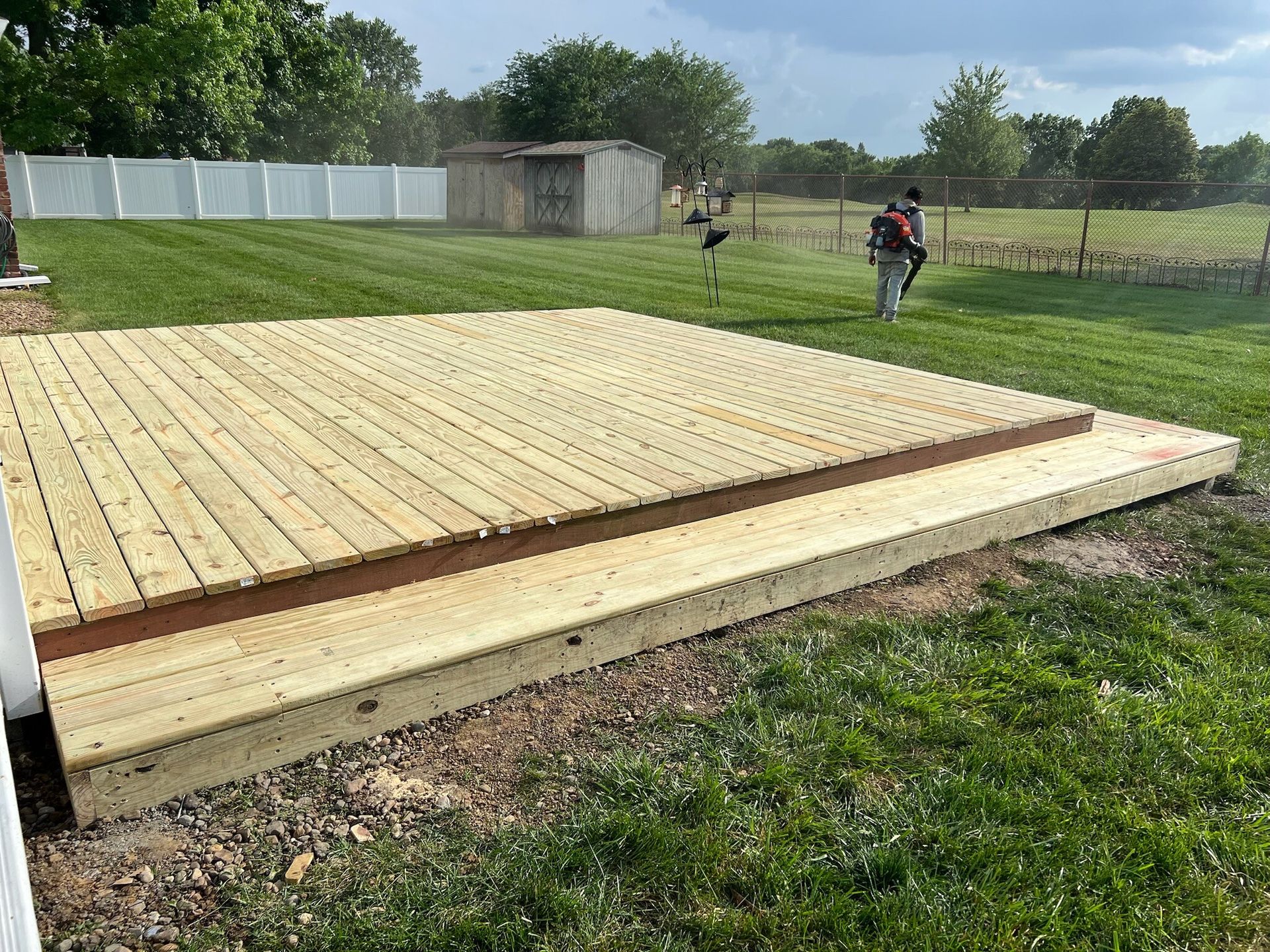 New wooden deck platform in a grassy backyard with two workers in the distance