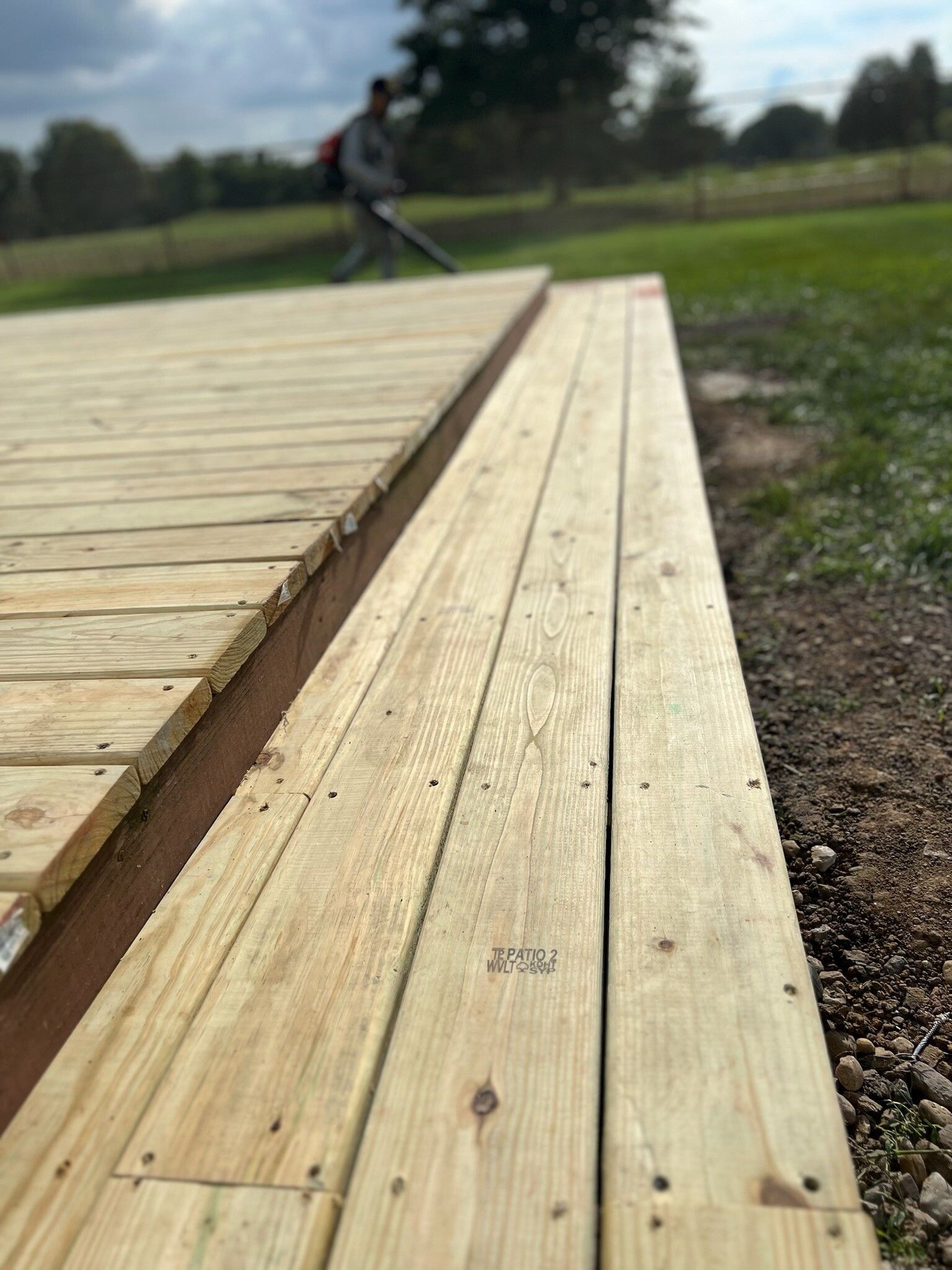 Wooden boardwalk with a person in the distance near a grassy field under cloudy skies