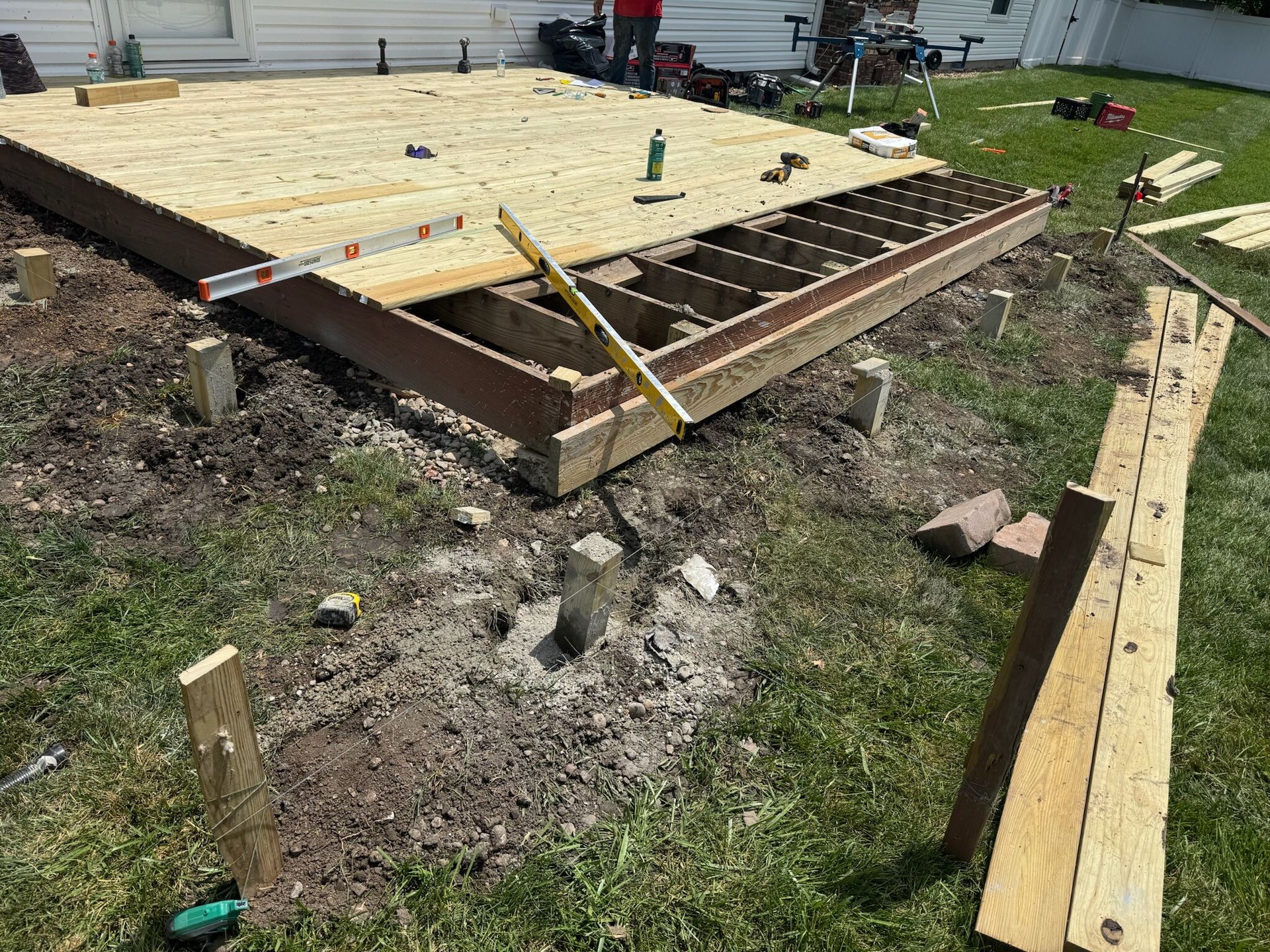 Partially built wooden deck framing in a yard, with lumber and tools nearby.