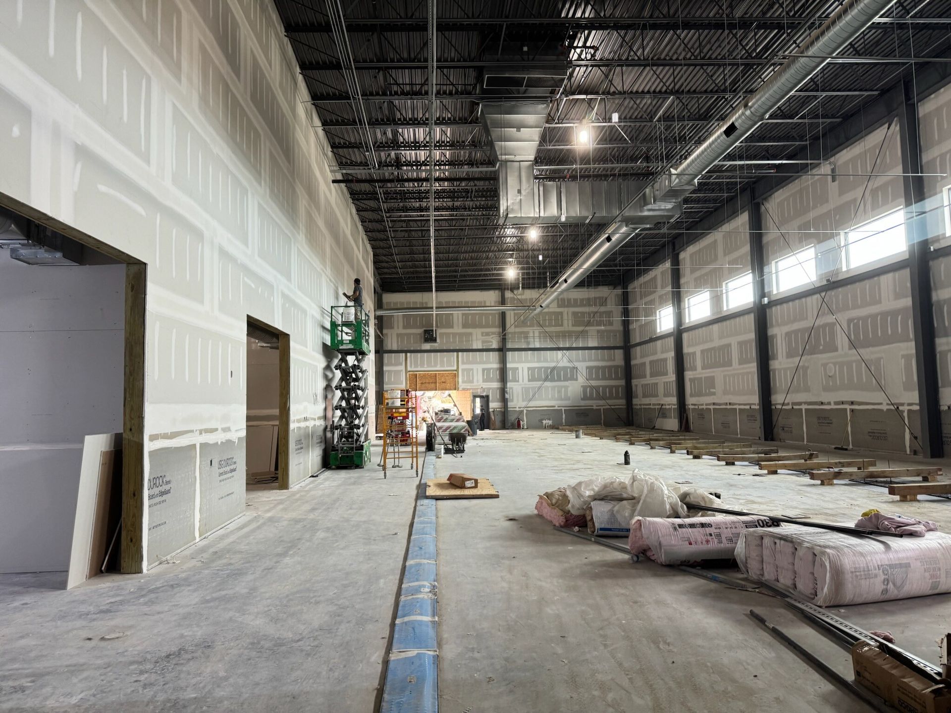 Large unfinished warehouse interior with construction materials, drywall walls, and exposed ceiling beams.