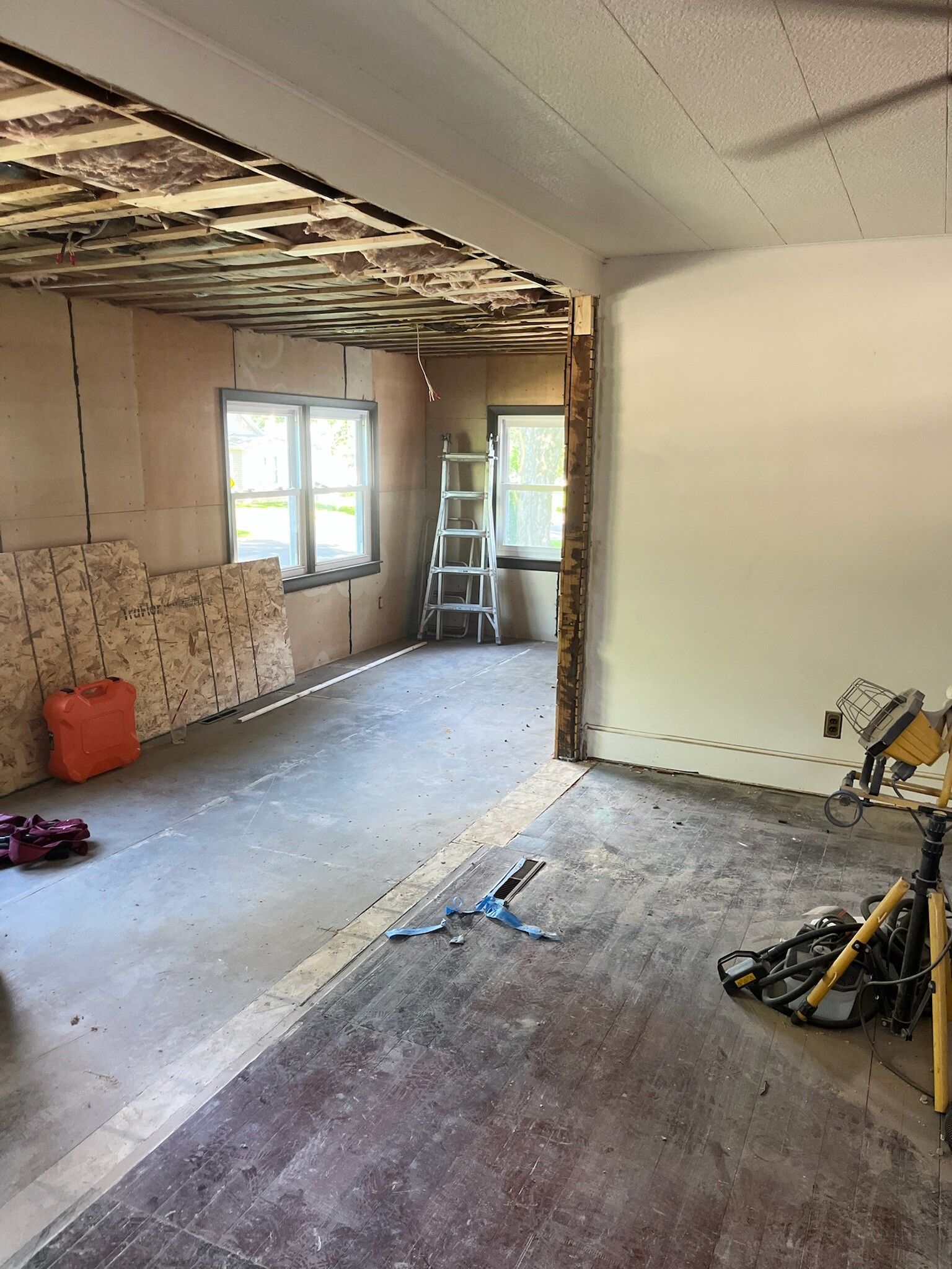 Partially renovated room with exposed ceiling, window, ladder, and tools on the floor