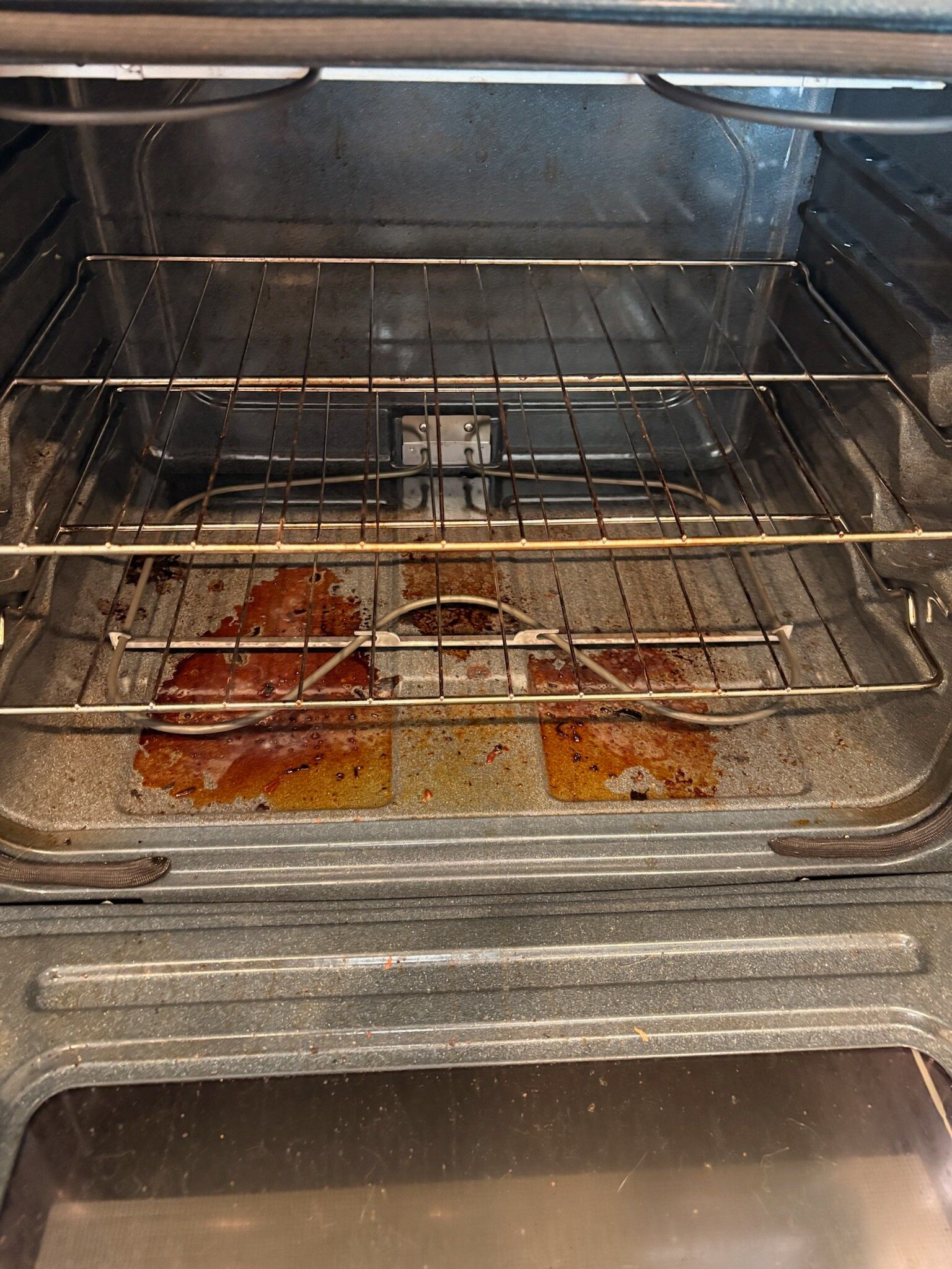 Dirty oven interior with wire racks and baked-on food spills on the bottom tray