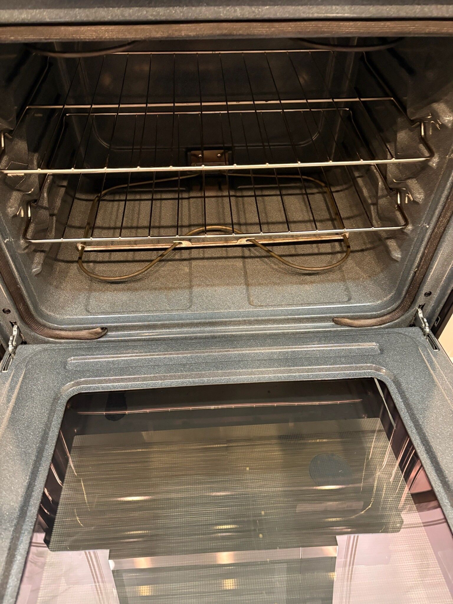 Open oven with metal racks and a baking tray inside, showing a charred bottom panel