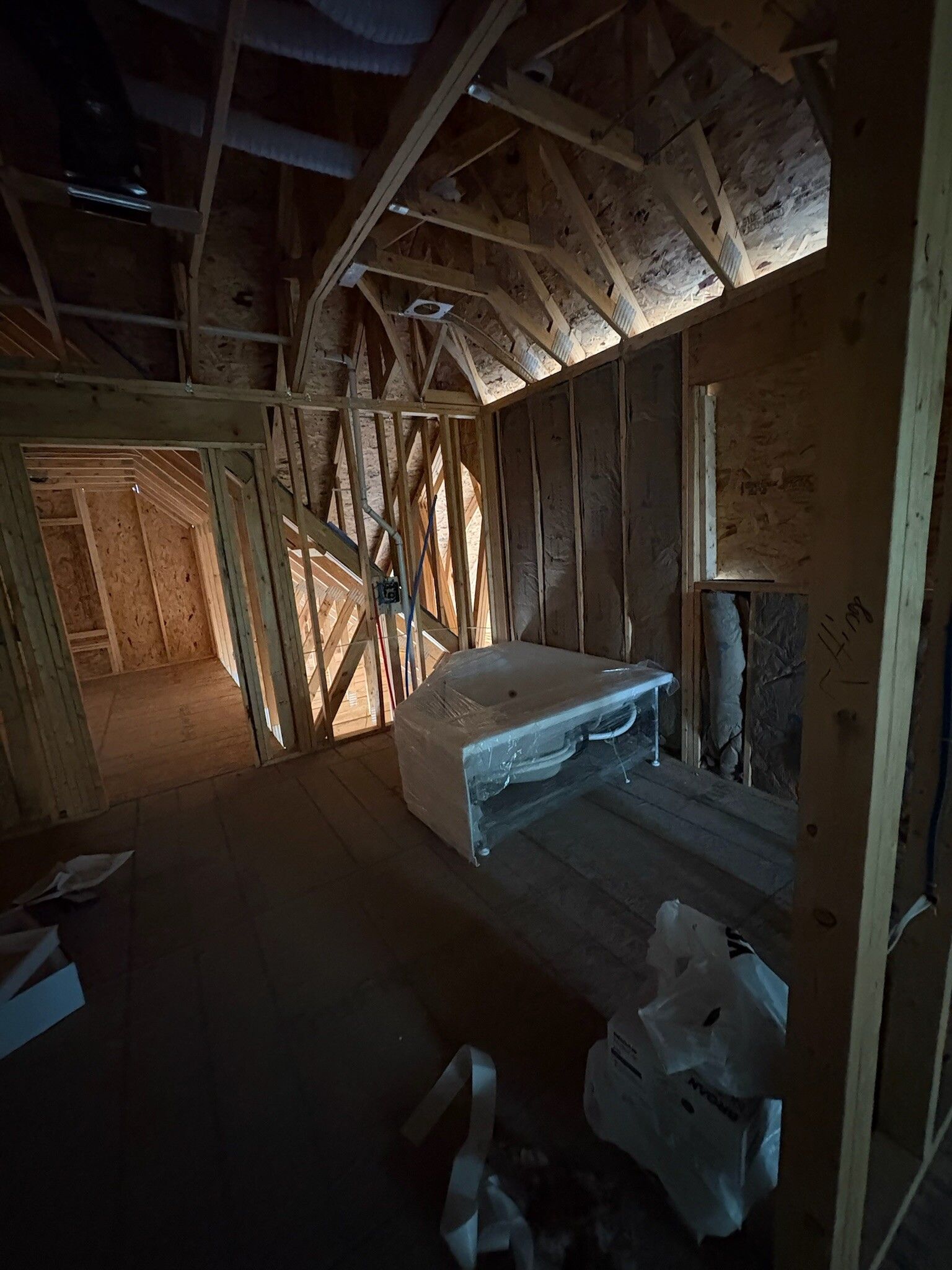 Unfinished attic with exposed wooden rafters, insulation, and a workbench in dim light.