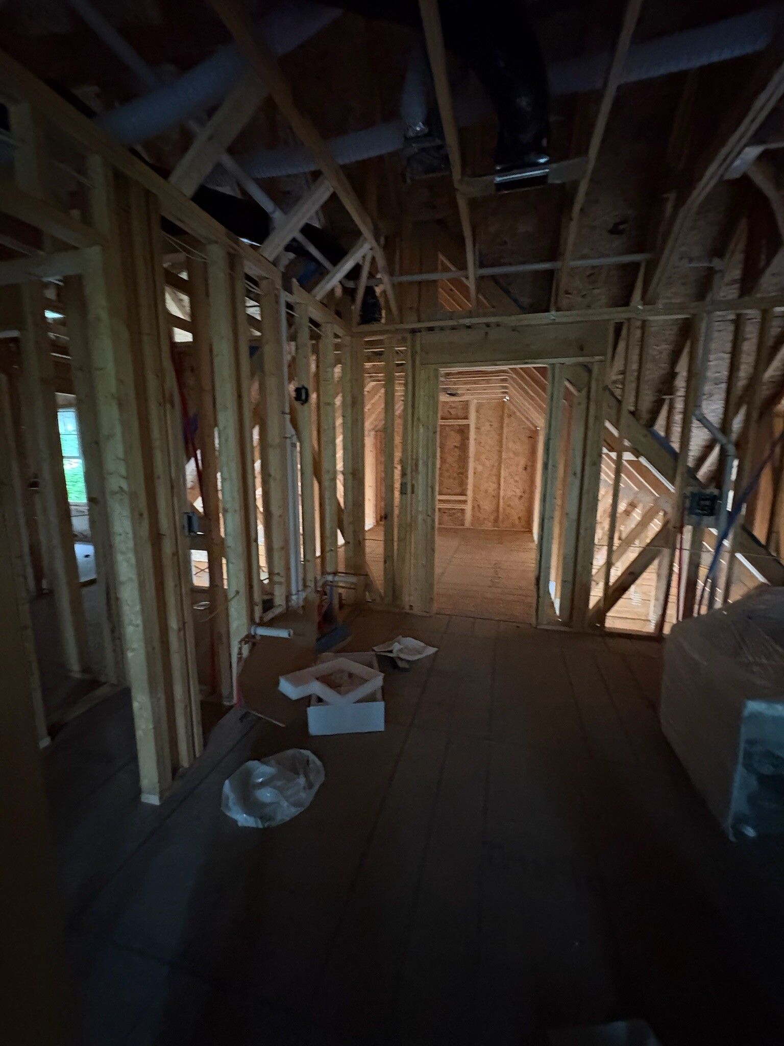 Unfinished house interior with exposed wooden framing, dark floor, and construction materials scattered on the ground.