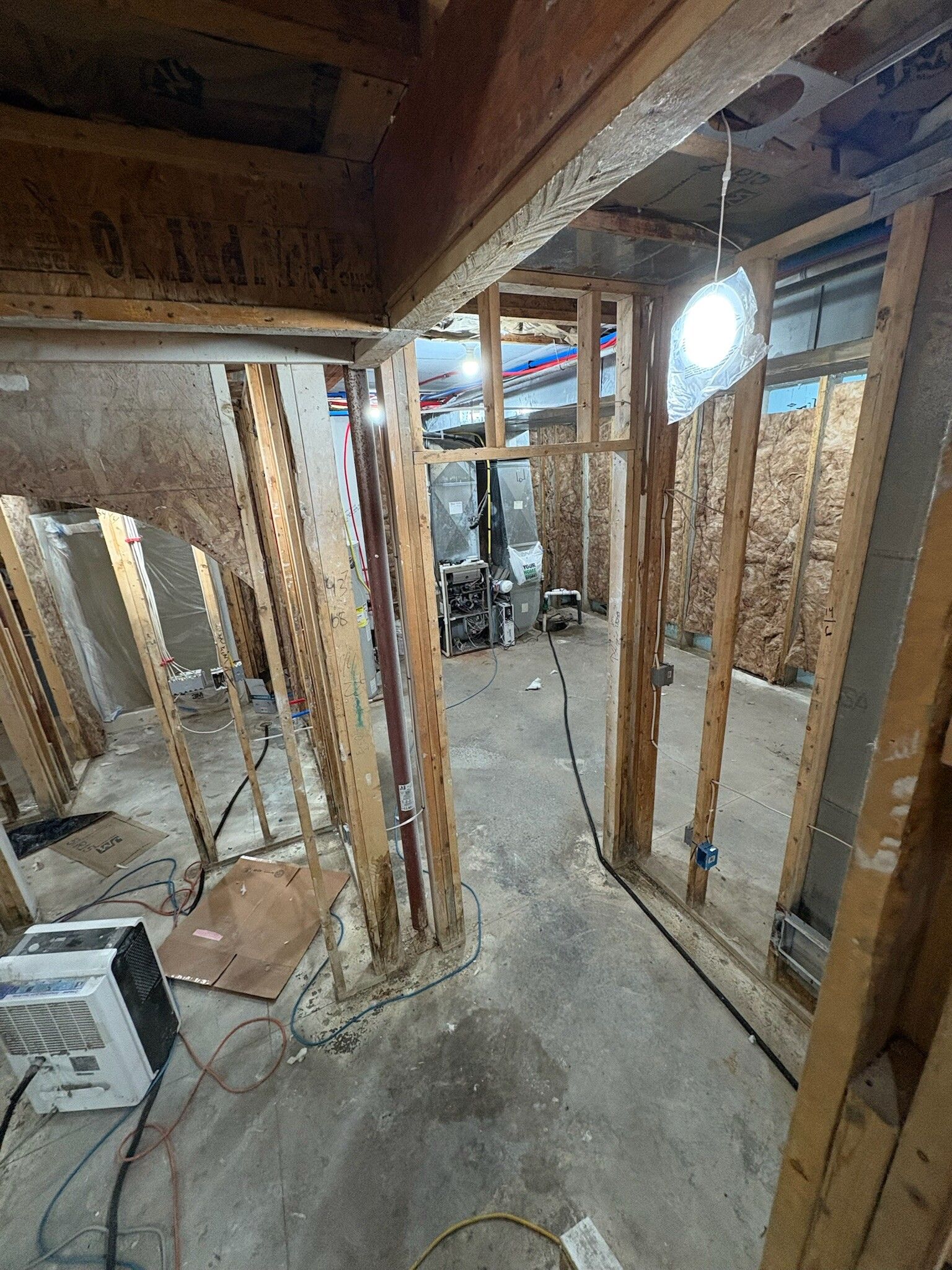 Basement under construction with exposed wooden framing, concrete floor, and tools in a narrow hallway