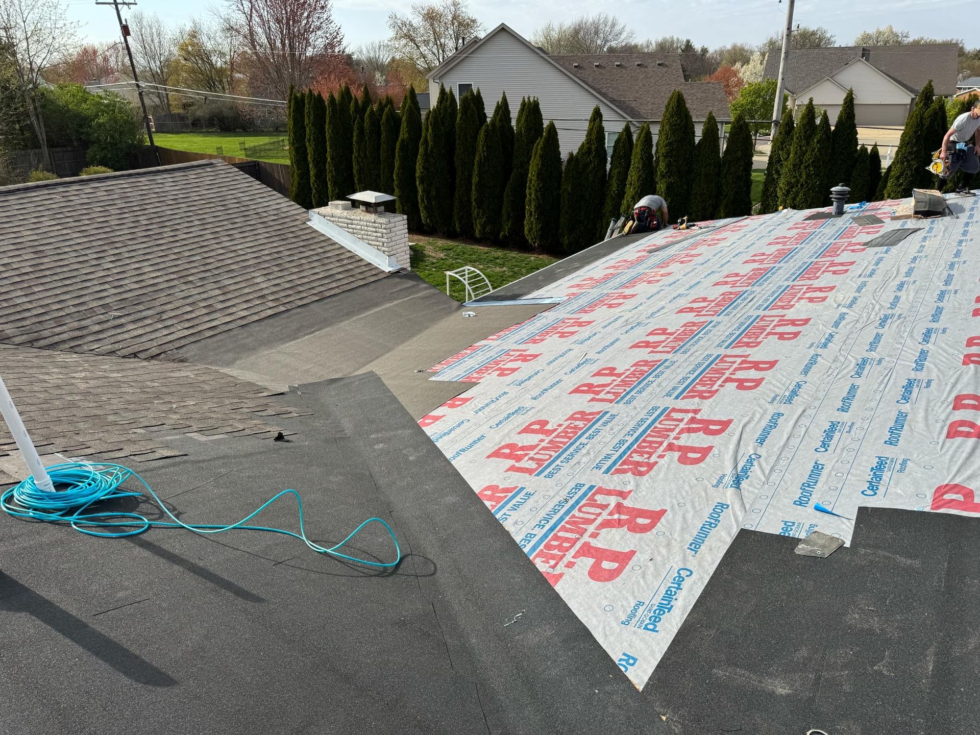 Roof under repair with underlayment sheets and blue rope on a sloped residential roof