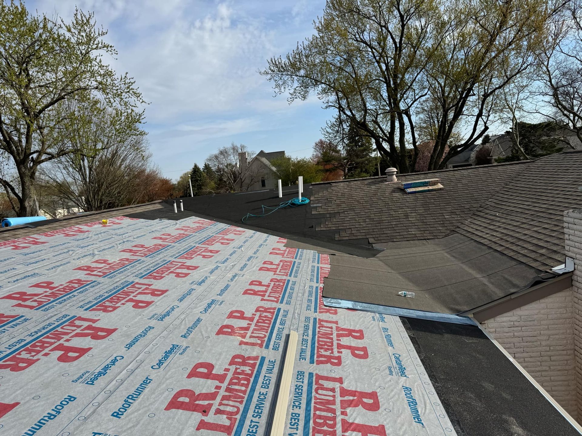 Roof under construction with red-and-white underlayment, trees, and a partly cloudy sky