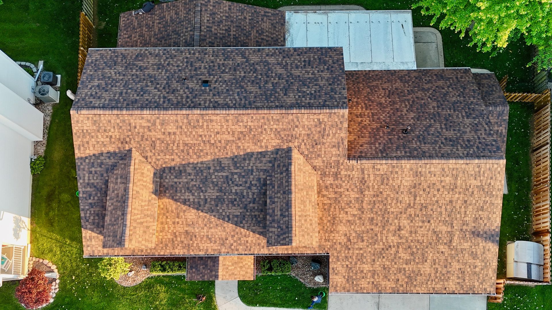 Aerial view of a house with a brown shingle roof and surrounding lawn, seen from above.