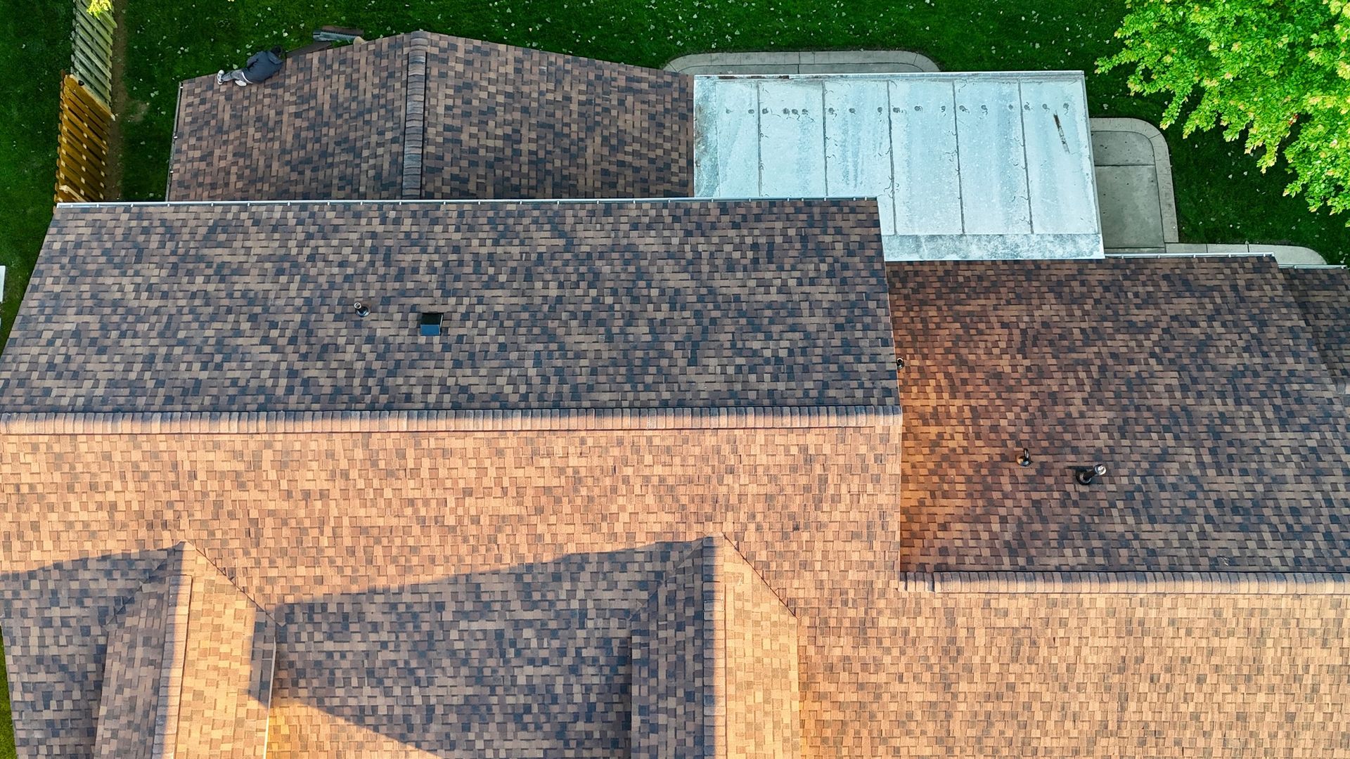 Aerial view of several weathered rooftops with gray shingles and a white metal roof amid greenery
