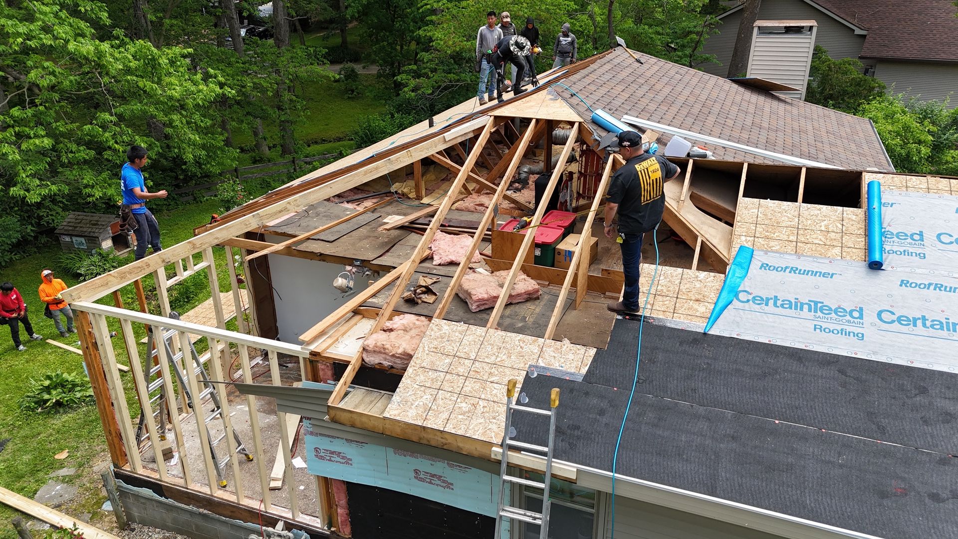 Roofing crew framing a house roof with plywood and trusses on a wooded hillside