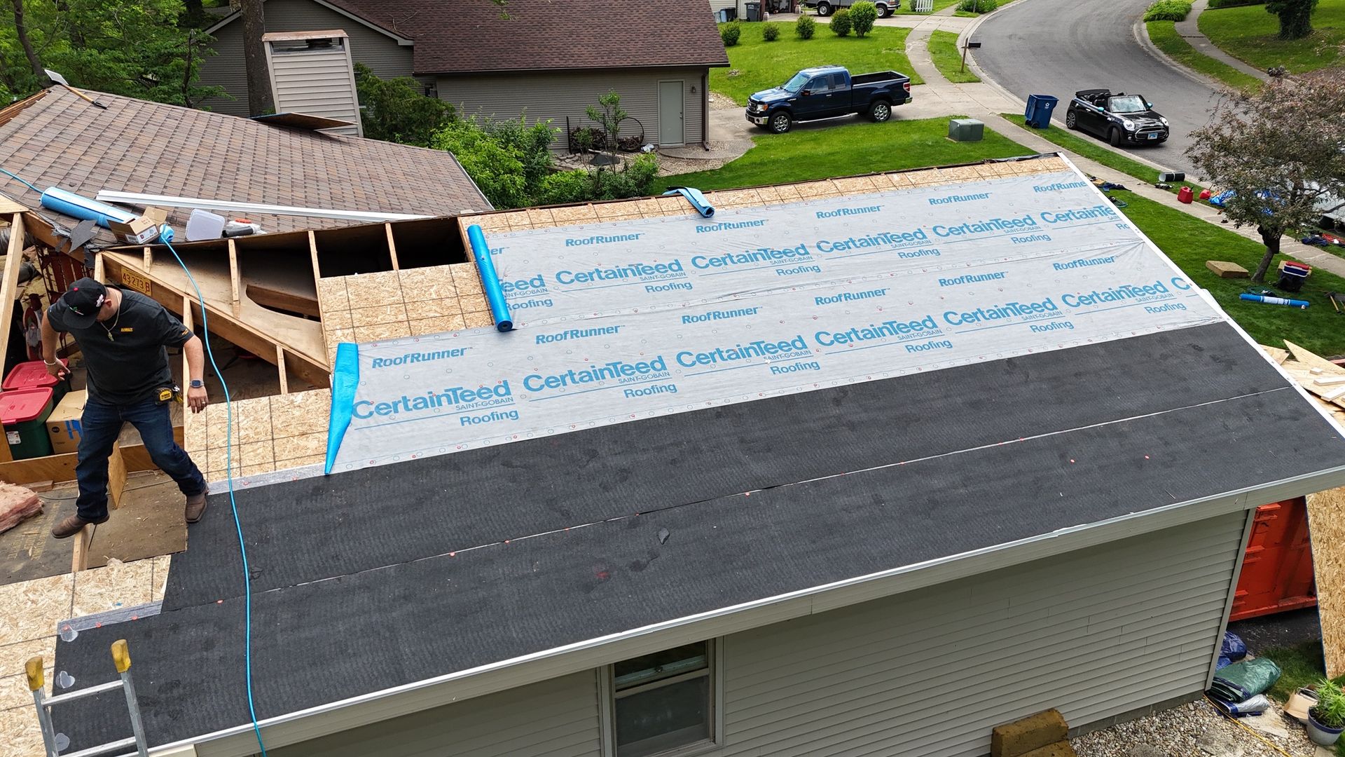 Workers replacing a shingle roof, with underlayment exposed and ladders on a suburban house
