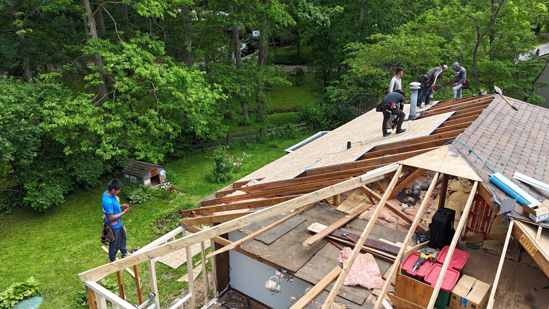 Collapsed roof with people assessing damage beside a wooded area