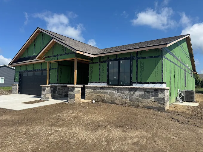 New green house with stone accents and a front porch under a clear blue sky