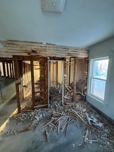 Partially demolished room with exposed studs, debris on the floor, and a window on the right
