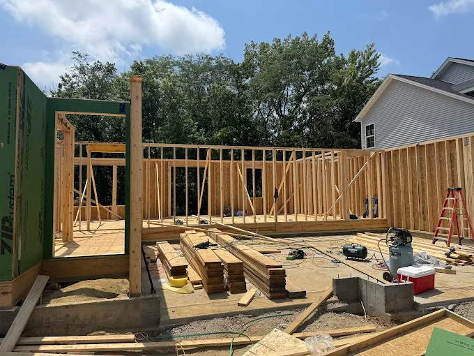 Partially built house frame with lumber, tools, and ladders on a sunny construction site