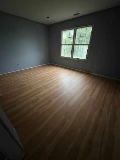 Empty room with gray walls, light wood floor, and a window letting in daylight.