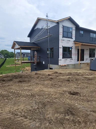 Partially built gray house with unfinished dirt yard and small covered porch