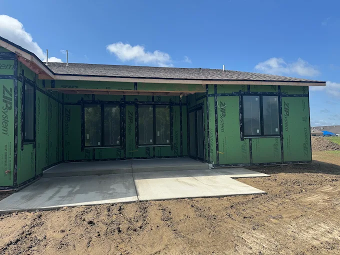 Partially built green house exterior with concrete driveway under a blue sky