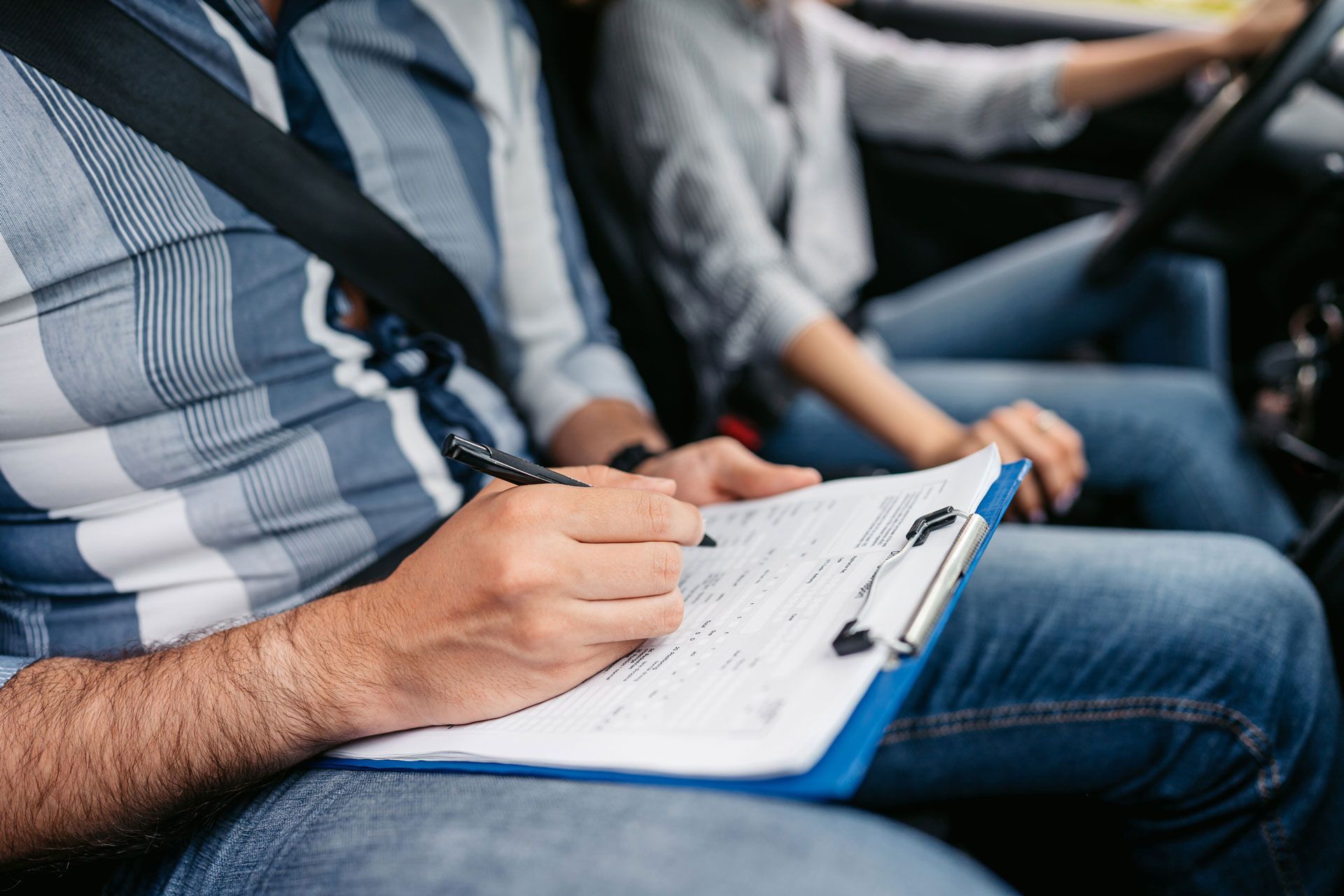 A man is writing on a clipboard while sitting in a car