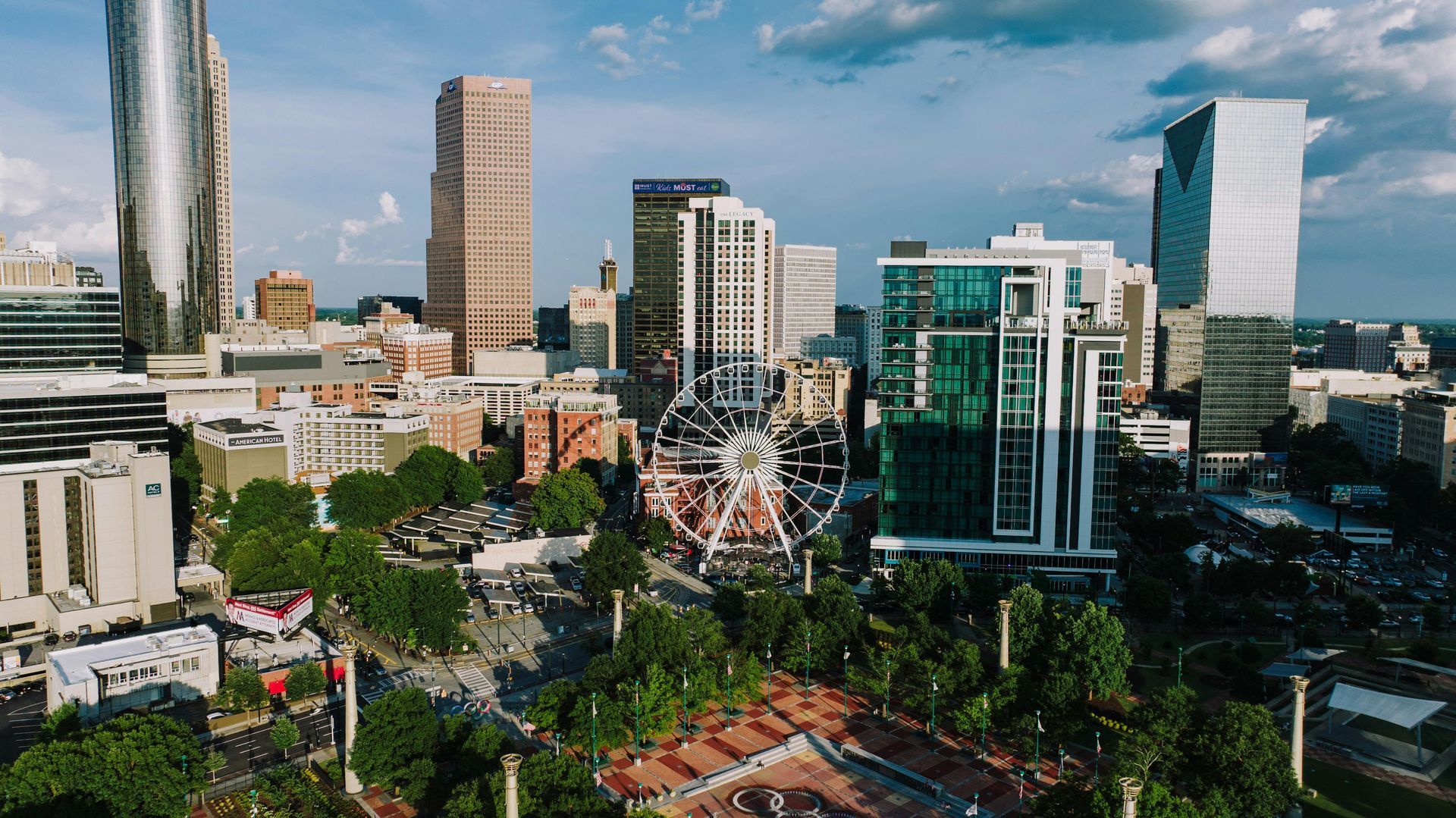 City skyline with modern high-rises, a ferris wheel, and a green park under a blue sky.