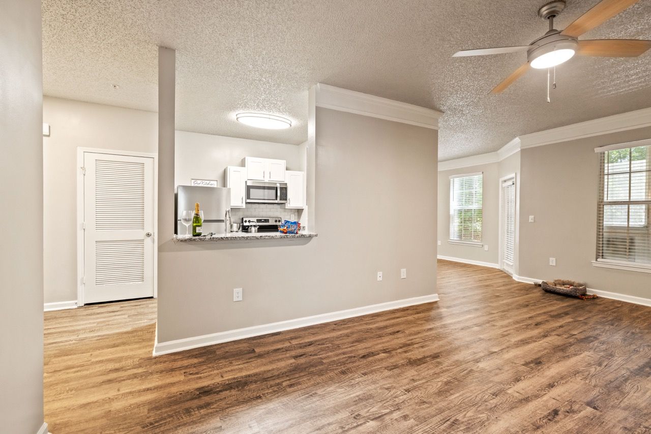 Open-concept living area with a kitchen bar, white cabinets, wood-look flooring, and a ceiling fan.